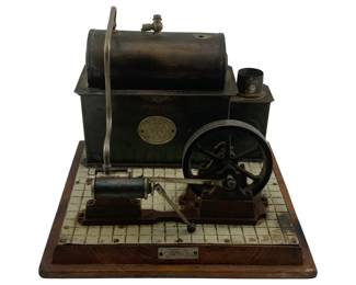 920 - Comet Steam Engine Toy 5"x8"x8" (Description): Comet steam engine toy mounted on a wooden base with tiled platform. Features a dark metal boiler with cylindrical top, flywheel mechanism, and piston assembly. The engine bears a decorative brass medallion with the Comet logo. A metal nameplate reading "COMET" is affixed to the front edge of the wooden base. Measures 5" x 8" x 8". Used as is electric/electronic/mechanical item. No guarantee all components, untested.