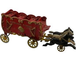 1192 - Vtg Cast Iron Overland Circus Wagon Toy (Description): Vintage cast iron horse-drawn circus wagon toy marked "Overland Circus" on the side. The wagon features red painted body with gold decorative scrollwork, harps, and horn motifs. Pulled by a team of two painted horses, one black and one white, mounted on yellow spoke wheels. The wagon also features yellow spoke wheels at the front and grey wheels at the rear. Measures 11" x 5" x 2.5".