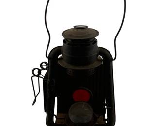 1116 - Antique Dietz Railroad Lantern 15"x6"x6" (Description): Antique Dietz railroad lantern featuring a black painted metal body with a wire bail handle. The lantern includes a red lens visible on one side and a clear lens, typical of railroad signal lanterns. Measures 15 inches tall by 6 inches wide by 6 inches deep.