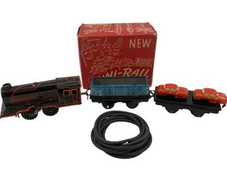 1180 - Vtg Uni-Rail Tin Train Set in Original Box (Description): Vintage Uni-Rail train set in its original red box. The set features a black and red tin lithograph locomotive with tender, a blue cargo car, and a flat car carrying two red automobiles. Includes coiled track. The original box displays playful cartoon graphics and reads 'New Uni-Rail' with cut-out features on the packaging.
