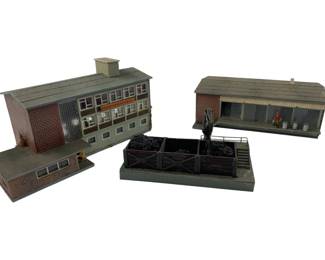 329 - Vollmer Display Train Set Buildings (Description): Vollmer display train set featuring three detailed HO scale buildings. The collection includes a two-story brick administration building with chimney, a corrugated roof warehouse or depot structure with figure and barrel accessories, and a coal yard with crane and storage bins. Buildings showcase realistic weathering and architectural detailing typical of European railway layouts. Measures 4" x 7" x 5.5".