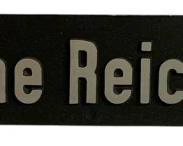 1075 - Deutsche Reichsbahn Metal Sign 23.5"x4" (Description): Deutsche Reichsbahn metal sign featuring the name of the German railway in silver lettering on a dark background. The rectangular sign has mounting holes at each corner. Measures 23.5 inches by 4 inches.