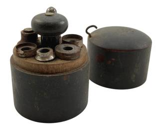 757 - Antique Punch Set in Wooden Canister 3.5" (Description): Antique tool punch set housed in a cylindrical wooden canister with a fitted lid featuring a wire loop handle. The set includes multiple metal punches of varying sizes arranged in holes around a central wooden knob handle. The canister has a dark painted finish with age-related patina and wear. Measures 3.5" in height.