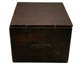 1204 - Antique Dark Wood Storage Box 9"x14"x11.5" (Description): Antique dark wood storage box with hinged lid and brass bail handle on the front. The box features a weathered patina with visible wear consistent with age, including surface scratches and paint residue. Metal hinges secure the lid. Measures 9 inches by 14 inches by 11.5 inches.