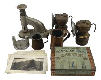909 - Mining Lamps, Cigarette Tin & Tools Lot (Description): An assorted lot of vintage items including two brass carbide mining lamps with hooks, a chrome industrial juice press or similar tool, two small copper measuring cups with handles, an M. Melachrino & Co. Egyptian Cigarettes tin, and a collection of vintage photographs.