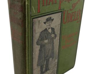 138 - That Printer of Udell's Harold Bell Wright (Description): That Printer of Udell's by Harold Bell Wright. This early edition features a decorative green cloth binding with pictorial cover illustration depicting a gentleman in period attire. The spine displays the title and author name in contrasting lettering. The book shows age-appropriate wear consistent with its vintage status.