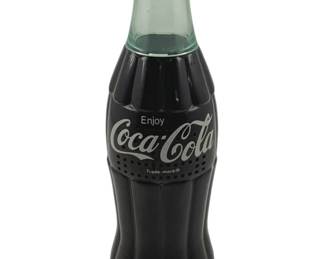 908 - Vintage Coca-Cola Bottle Radio 8" (Description): Vintage Coca-Cola bottle radio measuring 8 inches tall. This novelty radio is designed to look like a classic Coca-Cola contour bottle, complete with a silver bottle cap top and the iconic "Enjoy Coca-Cola" logo and Trade-mark branding. The radio features a speaker grille with small perforations on the lower portion of the bottle design. A fun piece of Coca-Cola memorabilia that combines the brand's classic aesthetic with functional