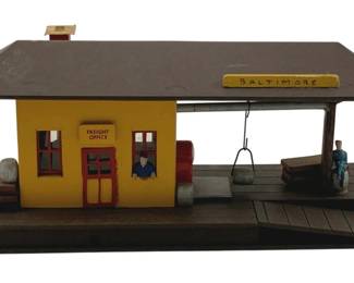 861 - Handmade Wood Lighted Station 5"x12"x14" (Description): Handmade wood lighted station featuring a yellow freight office building with red trim and doors, covered platform area with a "Baltimore" sign, and miniature figures and accessories. The station includes a loading dock with planks and various scenic details. Measures 5" x 12" x 14". Used as is electric/electronic/mechanical item. No guarantee all components, untested.