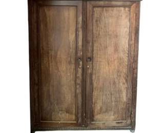 398 - 2 Door Wood Wardrobe 58"x43"x23" (Description): A traditional two-door wood wardrobe featuring paneled doors with round metal knobs and keyhole escutcheons. The piece has a flat top with subtle carved detailing along the crown molding. Measures 58 inches tall by 43 inches wide by 23 inches deep.