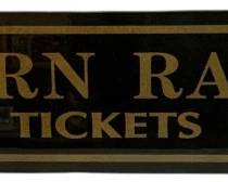 1061 - Southern Railroad Tickets Glass Sign 4.5"x27" (Description): Southern Railroad Tickets reverse-painted glass sign. This decorative piece features gold lettering on a black background with gold border detailing, reading "Southern Railroad Tickets." The sign has a reflective, mirrored quality typical of vintage railroad advertising signs. Measures 4.5" x 27".