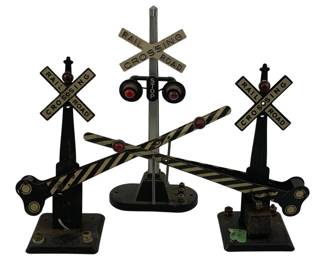 926 - 3 pc. Lot O Scale Metal Railroad Crossings 8" (Description): Three-piece lot of O scale metal railroad crossing signals and gates. The set includes a central crossing signal with dual lights, striped crossing gates, and a stop sign, flanked by two railroad crossing signals each featuring crossbuck signs and signal lights mounted on black painted metal bases. These vintage train accessories feature authentic detailing with black and yellow striped gates and red signal lights. Measures 8 inches