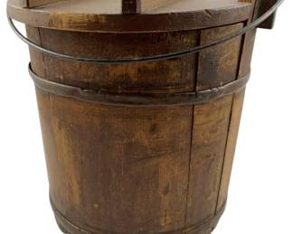 120 - Vintage Wooden Firkin Bucket 9"x9"x8" (Description): Vintage wooden firkin bucket featuring traditional staved construction with metal banding. The bucket includes a wooden lid with a raised wooden handle and a wire bail handle attached to the sides. The piece displays a warm, aged patina consistent with antique use. Measures 9 inches by 9 inches by 8 inches.