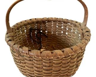 72 - Primitive Woven Splint Basket w/Handle (Description): Primitive handwoven splint basket featuring a sturdy bent wood handle. The basket displays traditional woven construction with natural wood tones showing an aged patina consistent with antique craftsmanship. The rounded form and open weave pattern are characteristic of 19th century utilitarian baskets. Measures 12" x 13".