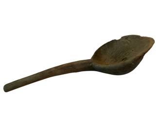 81 - Very Primitive Dough Bowl w/ Handle (Description): A very primitive hand-carved wooden dough bowl with an integrated handle. This rustic piece displays a deep, weathered patina consistent with age and extensive use. The bowl features a rounded, scalloped bowl section that transitions into a long, tapered handle. The wood shows natural wear, splits, and an organic coloration ranging from warm brown to grayish tones. Measures 6" x 28" x 9.5".
