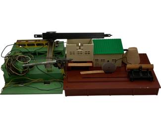 1147 - 2pc American Flyer Train Accessories Lot (Description): Two-piece lot of American Flyer train accessories. The lot includes a green painted metal crane or gantry structure with electrical wiring, and a sawmill building accessory featuring a cream-colored building with green roof, circular saw blade, log,and work platform mounted on a brown base. Both pieces are designed for model train layouts.