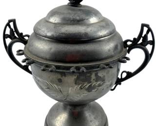 109 - Pewter Covered Dish w/Handles 8"x8"x6" (Description): Pewter covered dish with decorative handles featuring an ornate foliage design. The lid is topped with a sculptural fruit finial. The body displays etched leaf motifs and a beaded band detail around the midsection. The piece rests on a pedestal base and exhibits a lovely aged patina. Measures 8" x 8" x 6".