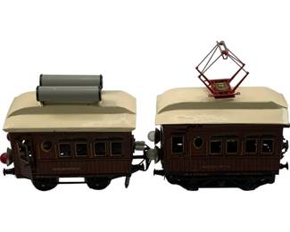 1199 - 2pc Marklin O Scale Train Cars Schlafwagen (Description): Two Marklin O scale train cars marked 'Schlafwagen' (sleeping car). These vintage tinplate passenger cars feature brown and cream coloring with detailed window arrangements. One car is equipped with a pantograph on the roof while the other has cylindrical roof fixtures. Both cars display the Marklin branding and feature coupling mechanisms at each end.