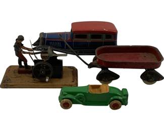 1128 - 4pc. Lot Antique Toys (Description): A collection of four antique toys including a painted tin lithograph automobile with red roof and blue body, a cast iron or painted metal wagon with red bed, a green painted rubber or composition open-top roadster with wooden wheels, and a painted tin mechanical figure of a man operating machinery mounted on a rectangular base. The pieces show wear consistent with age and play use, representing various toy manufacturing styles