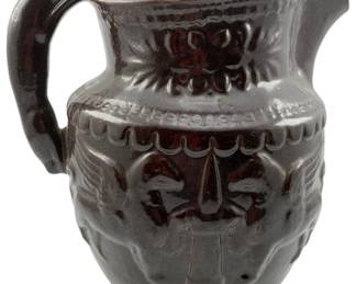 102 - Glazed Terracotta Figural Pulque Pitcher (Description): Glazed terracotta figural pulque pitcher featuring a rich dark brown glaze with traditional Mexican folk art motifs. The pitcher displays raised decorative elements including floral designs on the upper band and figural scenes on the body. Features a curved handle and spouted rim typical of traditional pulque vessels. Measures 9.25" x 10" x 7".