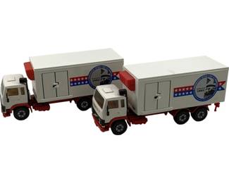 1175 - 2pc Siku 1982 Volvo Box Trucks Original (Description): Two original Siku 1982 Volvo box trucks in white with red and blue patriotic graphics featuring stars and stripes design. Each truck displays the Volvo 1982 logo on the trailer. Die-cast metal construction with plastic components. Measures 2.75" x 6" x 2".