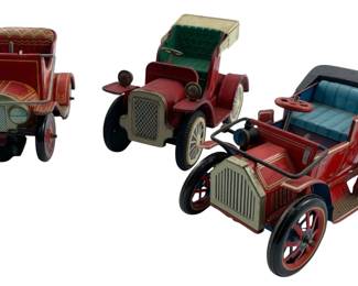 210 - Three Vintage Tin Litho Toy Antique Cars (Description): Collection of three vintage tin lithograph toy cars styled after early automobiles. Each features classic early 1900s automobile styling with colorful lithographed details, padded seat designs, rubber wheels, and metal trim accents. The cars display red body colors with varying decorative patterns and colored canopy tops. Measures 4"x3"x7".