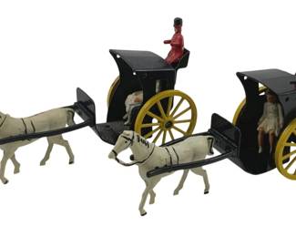 875 - 2pc Lot Metal Horse & Buggy w/ Riders 4" (Description): A pair of vintage painted metal horse and buggy toys, each featuring a white horse pulling a black carriage with yellow spoked wheels. Each buggy includes a driver figure dressed in red with a black top hat, and a passenger seated inside. These charming miniature carriages showcase classic Victorian-style hansom cab designs. Each measures approximately 4 inches.