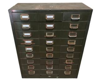 1218 - Vtg Industrial Metal Filing Cabinet (Description): Vintage industrial metal filing cabinet featuring 27 drawers with metal label holders. The cabinet has an olive green finish with visible patina and wear consistent with age and use. Original label cards remain in many of the drawer pulls. Measures38" x 31" x 13".