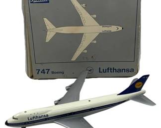 1215 - Schuco Lufthansa Boeing 747 Plane w/ Box (Description): Schuco Lufthansa Boeing 747 model airplane with original box. The die-cast model features the classic Lufthansa livery in white with dark blue accents and the airline's crane logo on the tail. The plane displays fine detailing typical of Schuco collectible aircraft models. Includes the original gray illustrated box marked "747 Boeing Lufthansa" with the Schuco logo.