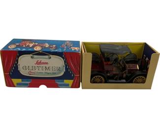 1184 - Schuco Old Timer 1909 Dakota in Box (Description): Schuco Oldtimer 1909 Opel Doktor Wagen in original box. This collectible tin toy car features a maroon body with gold-spoked wheels, a gray folding top, and detailed driver figure. The colorful original box displays theatrical red curtains and vintage automobile imagery from the Schuco Oldtimer series.