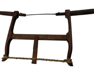 184 - Antique Wood Bow Saw 10"x19" (Description): Antique wood bow saw featuring a traditional H-frame construction with turned wooden handles. The saw retains its original metal blade stretched between the upper arms. A twisted rope tensioner runs along the bottom stretcher, used to adjust blade tension. The dark-stained hardwood frame shows authentic patina and wear consistent with age and use. Measures 10 inches by 19 inches.