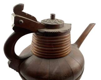 58 - 19th C. Norwegian Folk Art Spout Tankard (Description): A 19th century Norwegian antique folk art spout tankard crafted from dark stained wood. This traditional vessel features a bulbous staved body with turned horizontal ribbing at the base and neck. The tankard is fitted with a hinged lid decorated with carved geometric star motifs, a curved handle, and a protruding spout. The rich patina of the wood speaks to its age and use. Measures 14"x16"x11".