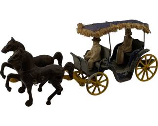 1127 - Vtg Cast Iron Horse & Buggy Toy 5"x11"x3" (Description): Vintage cast iron horse and buggy toy featuring two dark brown horses pulling a carriage with a fringed fabric canopy. The carriage is painted in blue and white with yellow spoked wheels and includes driver and passenger figures. The piece displays charming Victorian-era styling with decorative details throughout. Measures 5 inches by 11 inches by 3 inches.