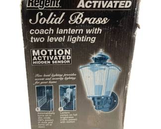 776 - Regent Motion Activated Light in Box (Description): Regent motion activated light, new in box. This solid brass coach lantern features two level lighting with a motion activated hidden sensor. The lantern automatically turns on in dim mode at dusk and off at dawn, with full brightness activating upon motion detection. Also operates in manual override mode. Model MBL200BK in black and brass finish. Used as is electric/electronic/mechanical