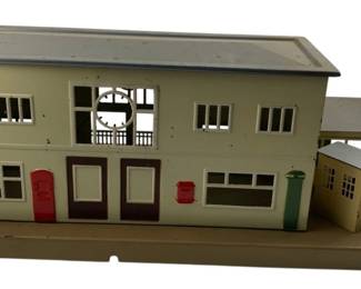 252 - Marklin Train Station 7"x19"x8" (Description): Featuring a two-story main building with multiple windows and doors, accompanied by smaller auxiliary structures on the platform base. Measures 7 inches by 19 inches by 8 inches.