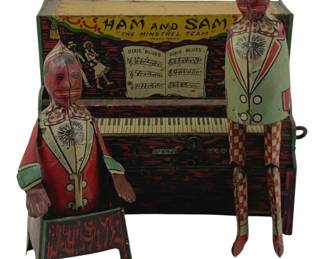 844 - Ham and Sam Minstrel Team Tin Litho Piano Toy (Description): Hamstrom's Ham and Sam "The Minstrel Team" tin lithograph wind-up toy featuring two figures seated at an upright piano. The colorfully decorated piece displays "Dixie Blues" sheet music on the piano's music stand, with a start/stop lever on the left. The figures wear matching outfits with checkered pants and decorative jackets in red, green, and white. Measures 7" x 5" x 5". Used as is electric/electronic/mechanical