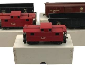 915 - 5pc Lionel HO Scale Trains w/ Boxes (Description): A collection of five Lionel HO scale train cars with original boxes. The lot includes two red N.Y.C. cabooses numbered 0047 and 0027, a black S.F. hopper car, a dark blue B&O hopper car numbered 0040, and a brown Pennsylvania boxcar. Each car measures approximately 2 inches by 6 inches by 1 inch.