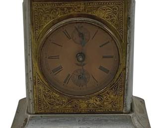 842 - Ant. Musical Mantle Clock 6"x5"x4" (Description): Antique musical mantle clock featuring a brass case with ornate scrollwork detailing surrounding the dial. The clock face displays Roman numerals with a secondary dial below. Topped with a carrying handle. Measures 6" x 5" x 4". Used as is electric/electronic/mechanical item. No guarantee all components, untested.