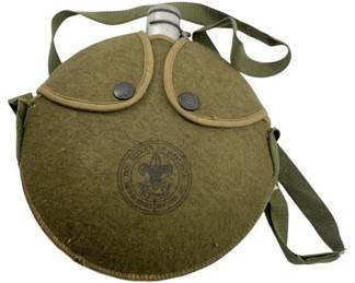 680 - Boy Scouts of America Canteen w/ Strap (Description): Boy Scouts of America canteen with olive green felt cover featuring the official BSA emblem. The canteen includes an adjustable carrying strap and metal cap. Measures 2 inches by 9 inches by 8 inches.