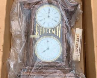 444 - Ridgeway Wall Clock in Box 24"x16"x6" (Description): Ridgeway wall clock in original box. This traditional style clock features dual dials - an upper clock face with Roman numerals and a lower calendar dial. The clock has a wooden case with decorative accents. Measures 24" x 16" x 6". Used as is electric/electronic/mechanical item. No guarantee all components, untested.