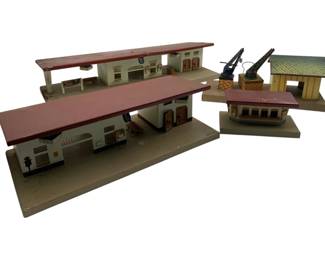 328 - Swiss Co. Wesa Train Station Set 3"x15"x5" (Description): Swiss Co. Wesa train station set featuring multiple painted tin lithograph buildings. The collection includes two long platform station buildings with red roofs, a smaller station building, a crane structure, and a small house with blue shingled roof. The buildings are mounted on rectangular bases and feature detailed printed architectural elements including windows, doors, and signage. Measures 3" x 15" x 5".
