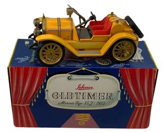 1207 - Schuco Oldtimer 1913 Mercer Type 35J w/ Box (Description): Schuco Oldtimer 1913 Mercer Typ 35J model car with original box. This vintage tin toy features a yellow body with red upholstered seats, brass-colored spoke wheels, and detailed mechanical components including headlamps, steering wheel, and engine.The model represents the classic 1913 Mercer automobile. Comes with the original decorative Schuco Oldtimer box featuring theatrical curtain design.