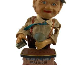 925 - Charlie Weaver Bartender Battery Operated Toy (Description): Charlie Weaver Bartender battery operated toy featuring the beloved character from the Jack Paar Show. The figure depicts the jovial bartender wearing a blue hat, cream-colored shirt with suspenders, and holding a bottle and glass. The lithographed tin base reads "Charley Weaver Bartender" with "Elsie Krack Was Here" printed inside a heart design. Measures 12" x 5" x 5".