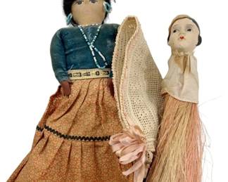 104 - Vtg Navajo Folk Art Dolls 11" (Description): Group lot of vintage Navajo folk art dolls measuring 11 inches. The collection includes a cloth doll dressed in traditional Navajo attire featuring a teal velvet blouse, turquoise beaded necklace, and printed cotton skirt with black rickrack trim. Also included is a smaller composition head doll with a crocheted shawl and raffia grass skirt, accented with a pink ribbon bow. Both dolls display charming handcrafted details