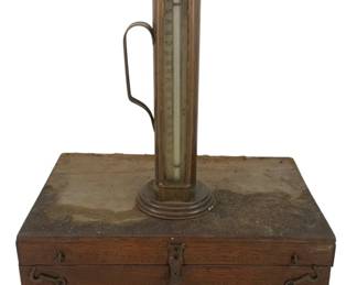 510 - Antique Thermometer Tool w/ Wood Box (Description): Antique thermometer tool with wood box. The thermometer features a brass casing with handle and stands mounted on a circular base. Comes with original wooden storage box with metal hardware. Measures 4 x 16.5 x 7 inches.
