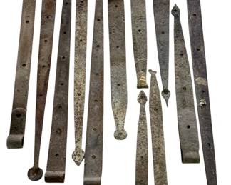 490 - Box Lot Antique Wrought Iron Strap Hinges (Description): Box lot of antique wrought iron strap hinges, likely from a cabin or barn. The collection includes approximately twelve hand-forged iron straps of varying lengths and decorative end designs, including spade, arrow, and rounded terminals. Each piece features multiple mounting holes and displays an aged, rustic patina consistent with period use. The longest piece measures 39 inches.