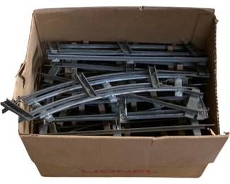1100 - Box Lot Lionel O Scale Train Tracks (Description): A box lot of O scale model train tracks in a Lionel branded cardboard box. The lot includes an assortment of curved and straight track sections with three-rail construction typical of O gauge trains. The metal tracks show a gray finish and include various pieces suitable for building or expanding a model railroad layout.