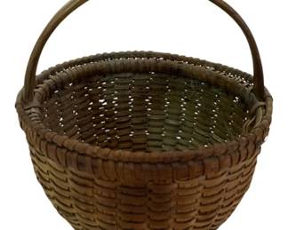 76 - Small Primitive Basket w/Handle 8"x6.5"x7" (Description): Small primitive woven splint basket with fixed bentwood swing handle. This charming country basket features a round form with a slightly tapered body and wrapped rim. The warm brown patina suggests age and use. Measures 8" x 6.5" x 7".