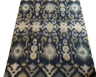162 - Blue Ikat Pattern Area Rug 96"x61" (Description): Area rug featuring an ikat-style pattern in shades of blue, cream, gold, and seafoam green. The design showcases repeating floral and geometric motifs on a deep blue ground. Measures 96 inches by 61 inches.