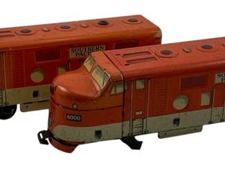 882 - 2pc Lot Marx Tin Litho Locomotives (Description): Two-piece lot of Marx tin lithograph locomotives in the Southern Pacific livery. Both engines are numbered 6000 and feature the classic red and cream color scheme with detailed lithographed windows, vents, and railroad markings. The streamlined diesel-style locomotives show vintage wear consistent with play use. Measures 3" x 9" x 2.5".