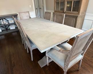 Restoration Hardware dining table with substantial pedestal base and stone-look top, paired with six upholstered dining chairs in a weathered oak finish.